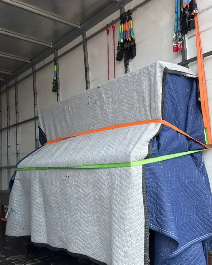 Furniture protected with moving blankets and securing straps inside a truck